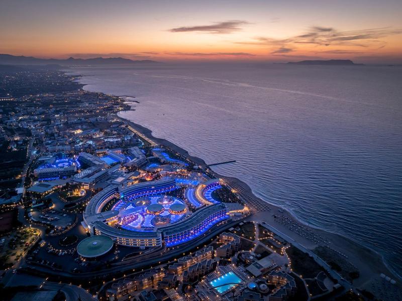 Vista aérea de un complejo costero iluminado al atardecer con playa y mar.