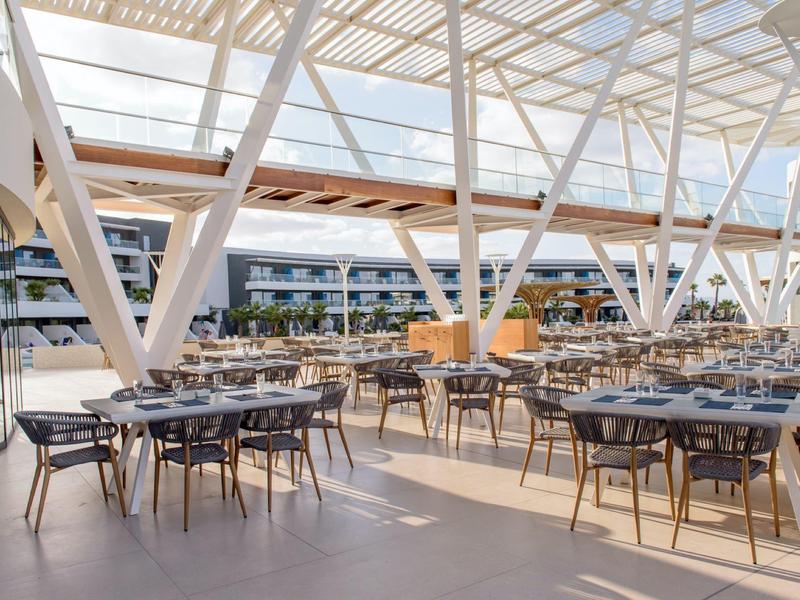 Restaurante de hotel moderno y luminoso con muchas mesas puestas bajo un techo de vidrio.