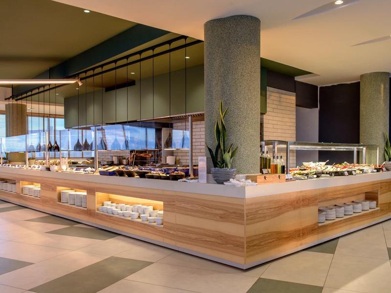 Buffet moderno con estación de comida en un hotel, decorado con madera clara y plantas.