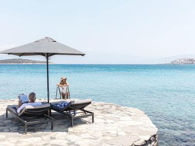 Deux personnes se détendent sur des chaises longues sous un parasol au bord de la mer.