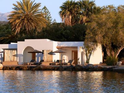 Villa blanche au bord de l'eau entourée de palmiers verts sous un ciel clair.