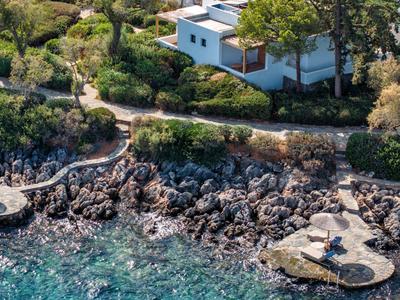Maison au bord d'une côte rocheuse avec eau claire et végétation environnante.