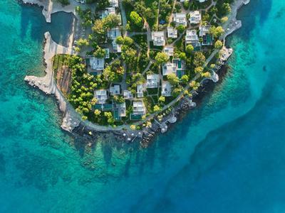 Vue aérienne d'une péninsule entourée d'arbres avec des bâtiments au bord de l'eau claire et bleue.