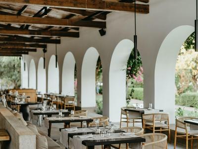 Terrasse couverte avec tables en bois et chaises, décorée de fleurs aux lampes suspendues.