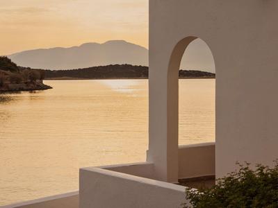 Murs blancs avec arche et vue sur un lac calme au coucher du soleil.