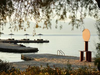 Section de plage avec eau calme, chaises longues et parasols, entourée d'arbres et de pierres.