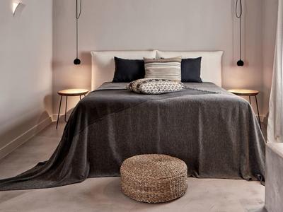 Chambre confortable avec dessus de lit gris, coussins et deux tables de chevet rondes avec lampes.