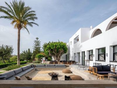 Area esterna moderna di un hotel bianco con posti a sedere e palme sotto un cielo limpido.