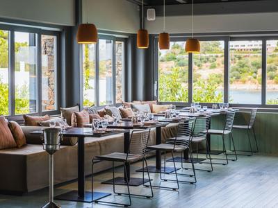 Area lounge d'hotel moderna con divani in pelle, tavoli e grandi finestre che si affacciano su aree verdi.