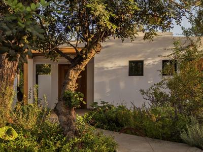 Maison blanche avec un arbre et un jardin au premier plan au coucher du soleil.
