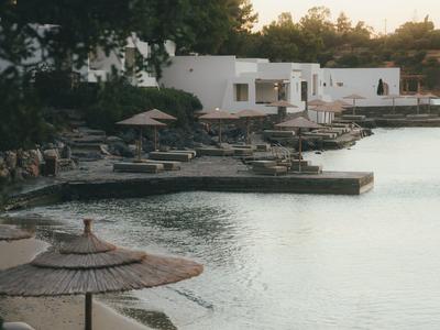 Une baie d'hôtel calme avec plage de sable, parasols et bâtiments blancs en arrière-plan au coucher du soleil.