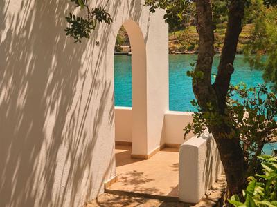 Vue sur la piscine à travers une arche blanche et des arbres dans un espace extérieur ensoleillé d'un hôtel.