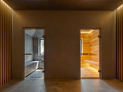 Couloir avec deux portes, à gauche salle de bain grise, à droite sauna en bois.