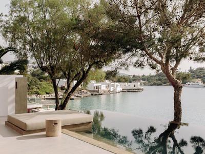 Terrasse moderne avec piscine surplombant une baie calme avec des arbres et des bâtiments en arrière-plan.