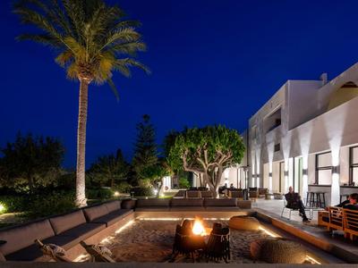 Hôtel moderne avec foyer extérieur, sièges confortables et palmiers la nuit.