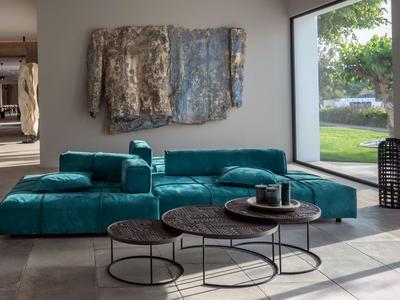 Salon moderne avec un grand canapé vert et deux tables rondes devant une grande fenêtre.