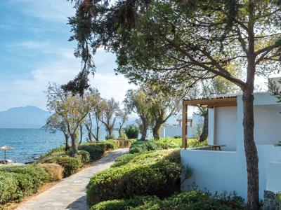 Un jardin d'hôtel avec un chemin pavé, des arbres et vue sur la mer en arrière-plan.