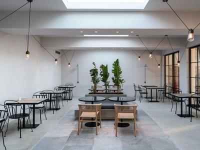 Salle à manger blanche avec grandes fenêtres, plantes et tables et chaises en bois minimalistes.
