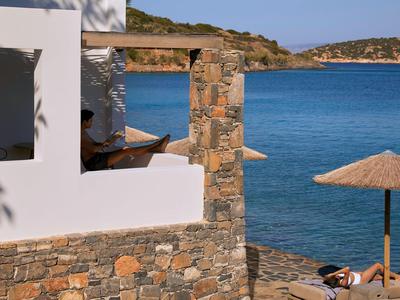 Vue sur la mer depuis une terrasse avec mur en pierre, bâtiment blanc et parasol.