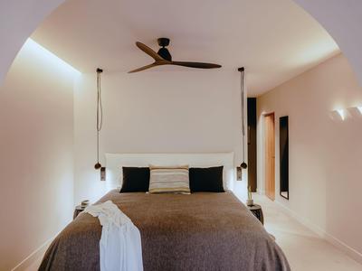 Chambre avec grand lit, ventilateur de plafond et design minimaliste aux tons chauds.