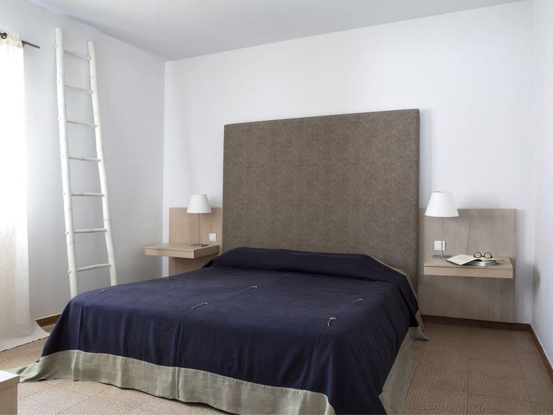 Chambre d'hôtel moderne avec tête de lit grise, couverture sombre et tables de chevet latérales.