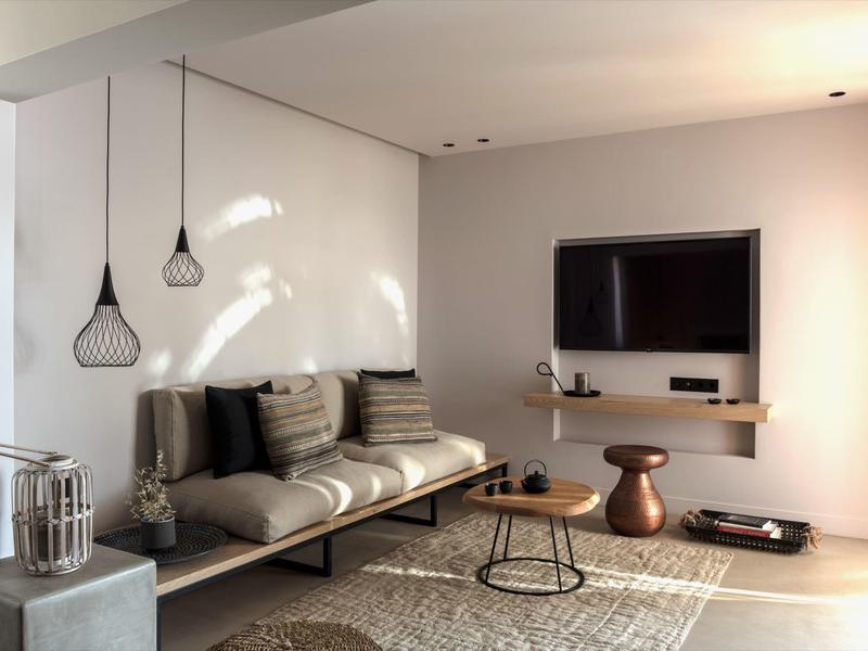 Chambre moderne d'hôtel avec canapé minimaliste, table basse et télévision murale dans une pièce lumineuse.