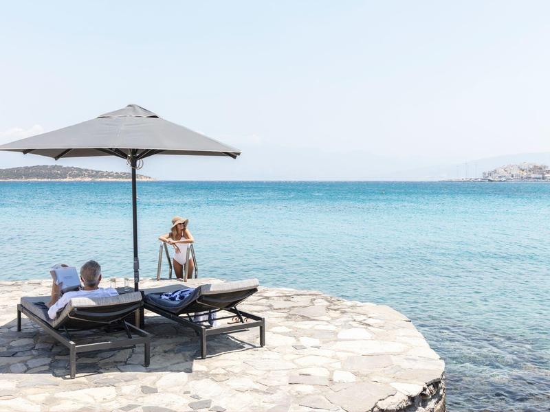 Deux personnes se détendent sur des chaises longues sous un parasol au bord de la mer.