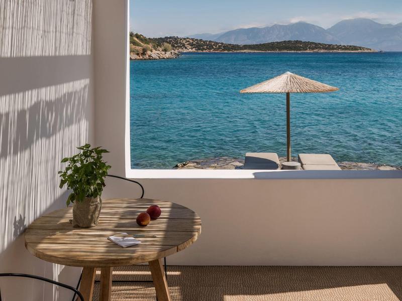 Vue sur la mer avec parasol et chaises longues depuis un balcon avec table et chaise.
