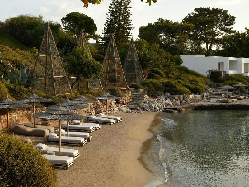 Plage avec transats et parasols à côté d'une mer calme et d'une végétation verte.