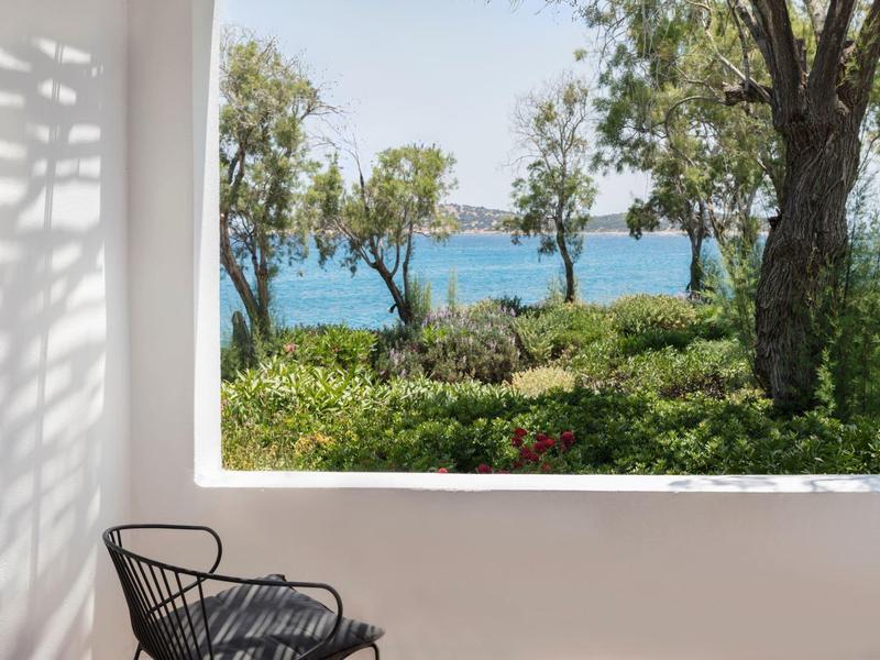 Vue depuis une terrasse avec chaise sur un jardin vert et la mer bleue à l'arrière.