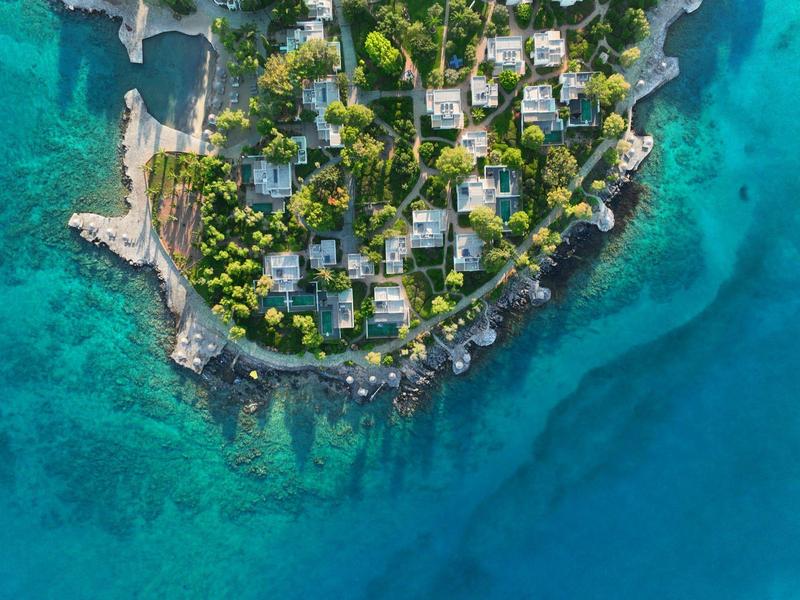 Vue aérienne d'une péninsule entourée d'arbres avec des bâtiments au bord de l'eau claire et bleue.