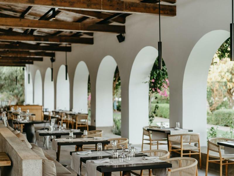 Terrasse couverte avec tables en bois et chaises, décorée de fleurs aux lampes suspendues.