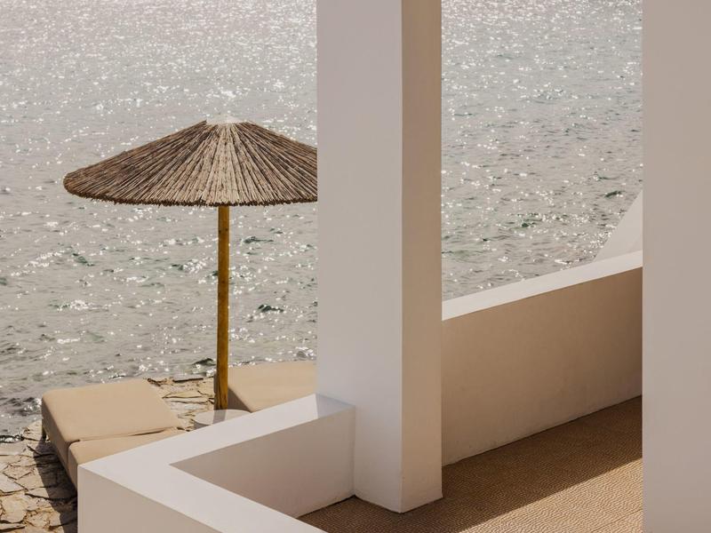 Vue d'un parasol en paille près de l'eau avec une architecture blanche au premier plan.