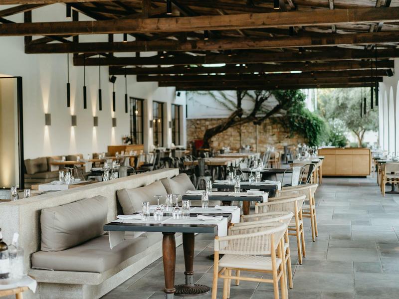Restaurant moderne et ouvert avec poutres en bois, banquettes grises et chaises en bois.