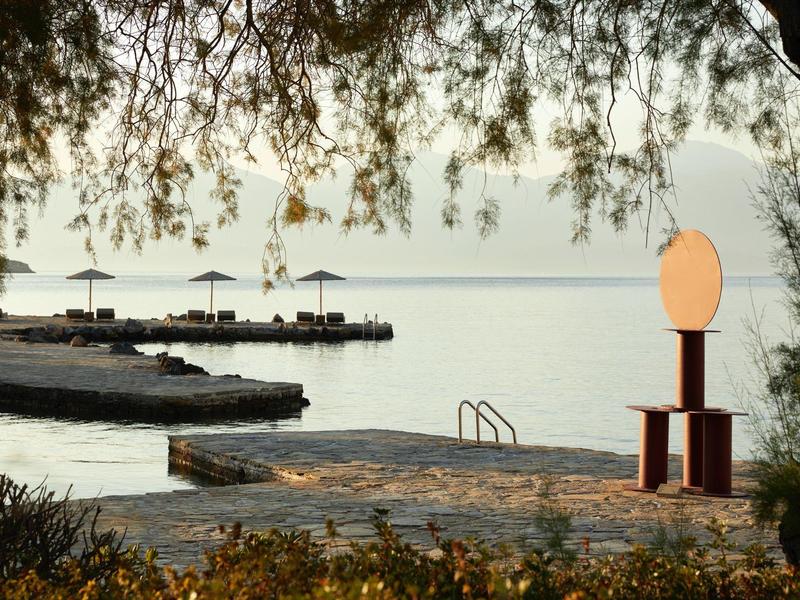 Section de plage avec eau calme, chaises longues et parasols, entourée d'arbres et de pierres.
