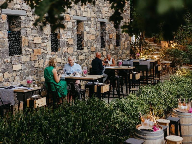 Des clients sont assis à l'extérieur à des tables près d'un mur en pierre dans un jardin verdoyant.