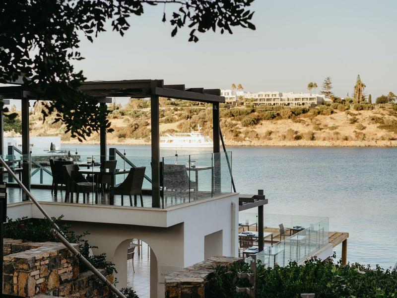 Terrasse d'hôtel avec tables et chaises au bord de l'eau, vue sur la côte