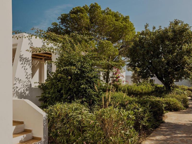 Sentier longeant une végétation dense à côté d'un bâtiment blanc sous un ciel clair.