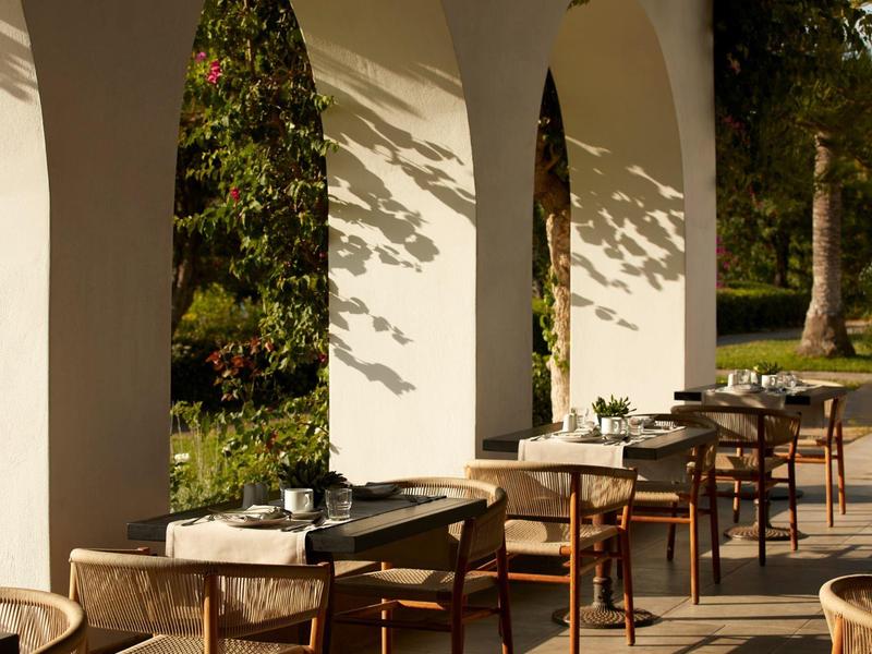 Terrasse de restaurant avec tables en bois et chaises sous des arches blanches en plein air.