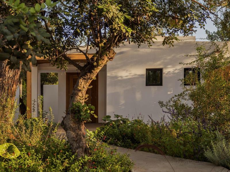 Maison blanche avec un arbre et un jardin au premier plan au coucher du soleil.