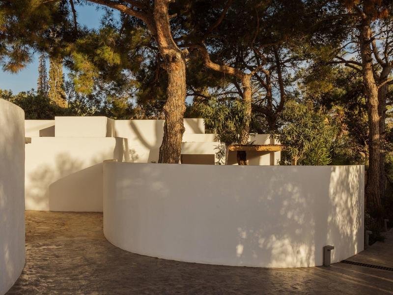 Des murs blancs courbes entourent un chemin avec des arbres et des ombres.