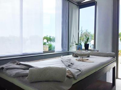 Hell eingerichteter Raum mit Massagetisch, Handtüchern und Pflanzen auf dem Fensterbrett.