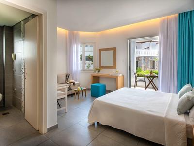 Helles Schlafzimmer mit Doppelbett, Schminktisch, blauen Vorhängen und angrenzendem Badezimmer.