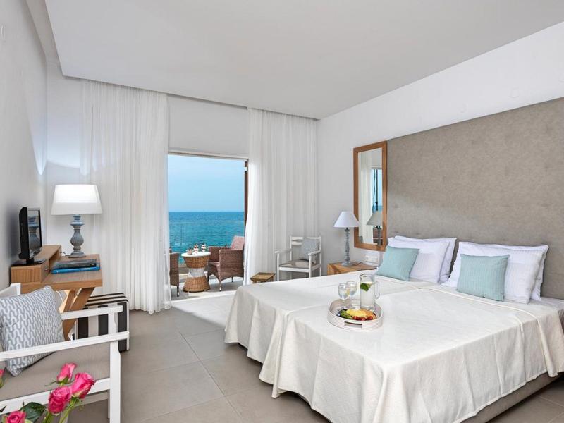 Camera d'hotel luminosa con due letti e balcone con vista mare.