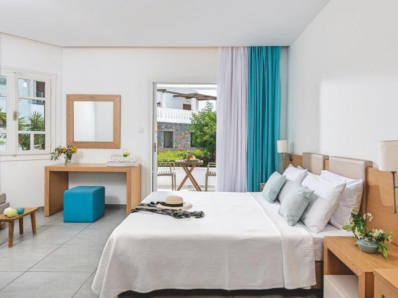 Camera d'hotel luminosa con letto matrimoniale, scrivania, specchio e balcone con zona salotto.