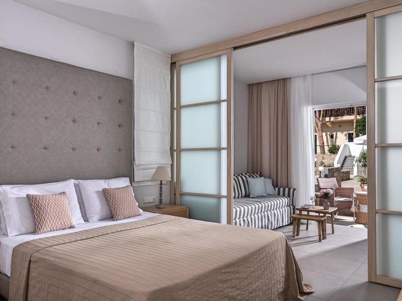 Camera d'hotel moderna con letto grande e area soggiorno adiacente con divani e tende.