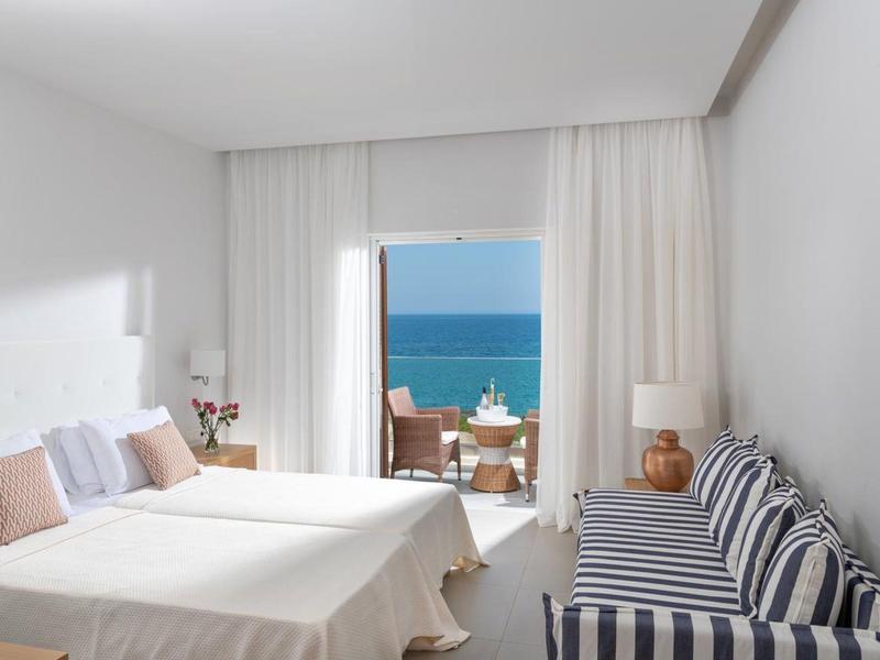 Camera d'hotel luminosa con letto matrimoniale, divano e balcone con vista mare.