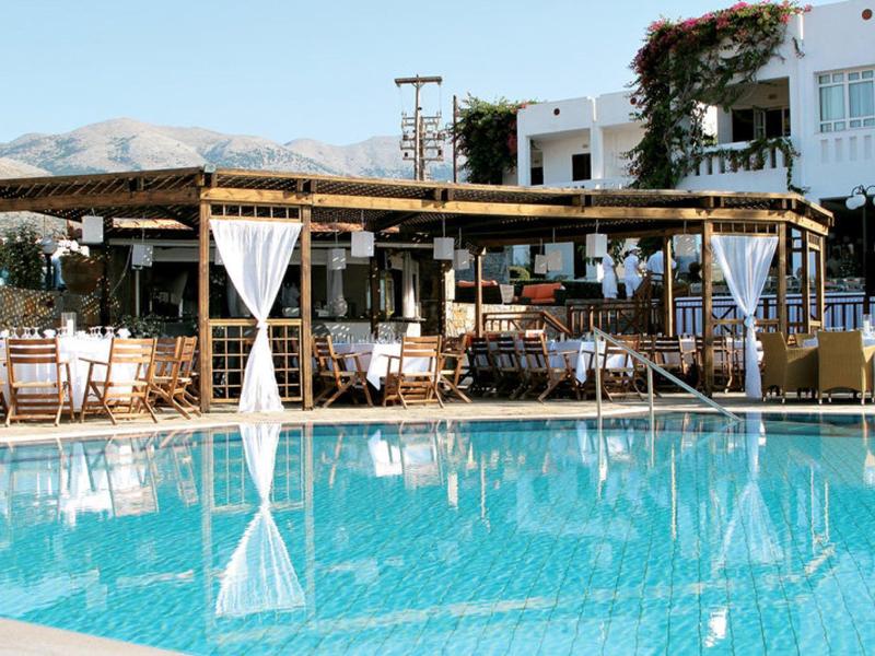 Grande piscina con acqua limpida davanti a un ristorante all'aperto con tetto in legno e edificio bianco.