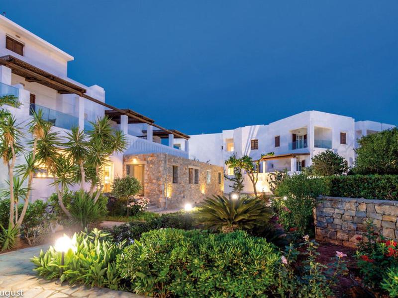 Scatto serale di un hotel illuminato con architettura mediterranea e giardino rigoglioso.