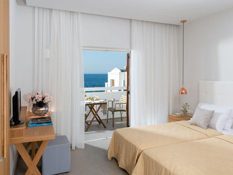 Camera d'hotel luminosa con letto matrimoniale e balcone con vista sul mare.